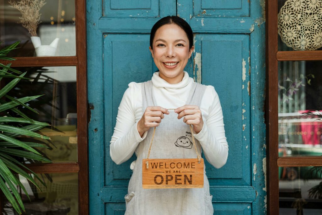 woman business owner holding open sign in front of cafe